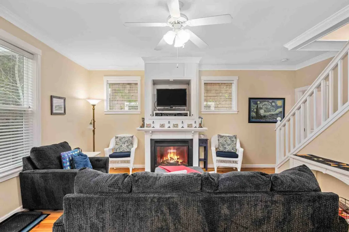 A warm and inviting living room featuring a cozy fireplace, plush sofa, armchairs, and a television. The space is designed for relaxation, socializing, and unwinding, giving a clear sense of comfort and togetherness.