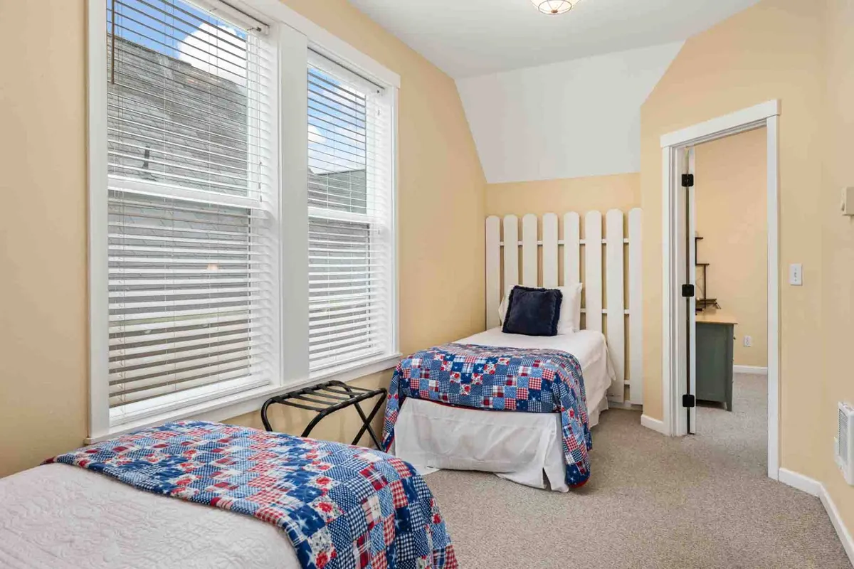 An inviting room showcasing twin beds with patterned quilts, large windows that flood the space with daylight, and a decorative wooden partition for added privacy. The space is cozy and open, ideal for restful relaxation or quiet reading.
