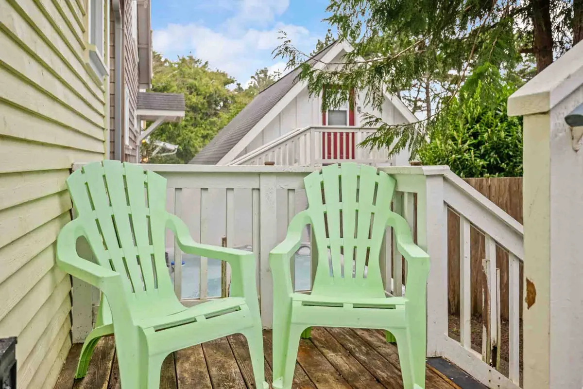This image shows an inviting wooden deck surrounded by lush trees, green Adirondack chairs arranged for conversation, and the house in the background. The scene captures both the natural greenspace and a functional outdoor seating area.