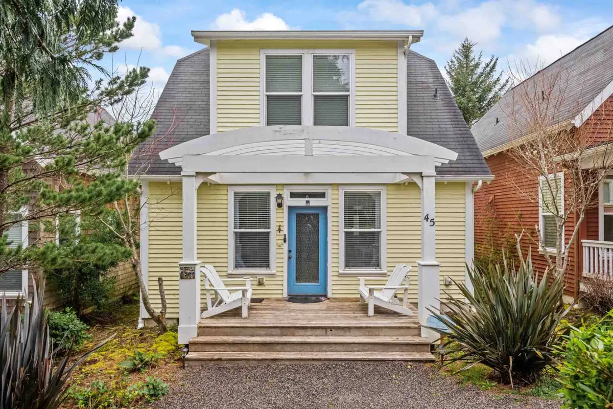 The image showcases the charming exterior of a two-story single family home with cheerful yellow siding, a bold blue front door, and a welcoming front porch overlooking lush landscape plants. The setting evokes relaxation and togetherness, inviting guests to gather on the porch for sunset views or enjoy peaceful mornings surrounded by nature.