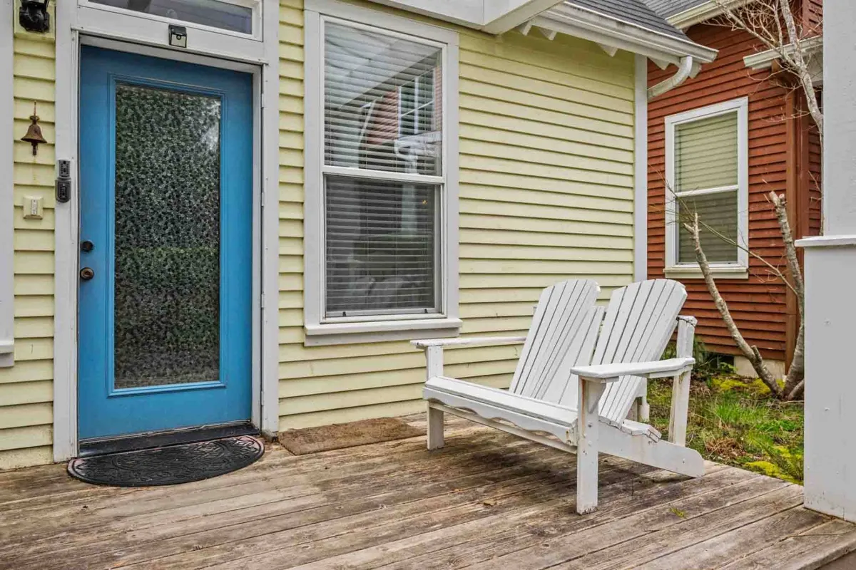 A cozy front porch with white Adirondack chairs and a blue door, set against a wooden porch backdrop. The area looks perfect for morning coffee or unwinding after a day out, epitomizing comfort and the ease of stepping right into nature.