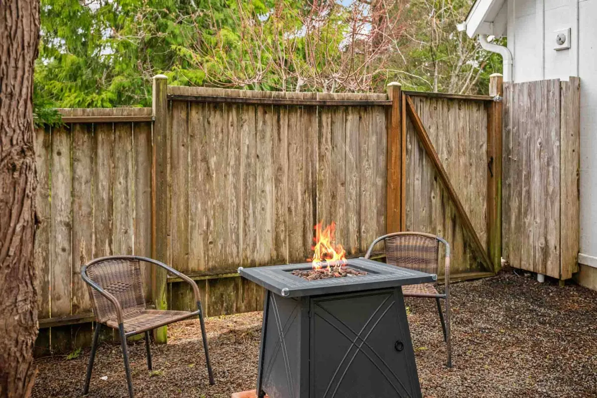 A welcoming outdoor gathering spot with a fire pit surrounded by wicker chairs and a wooden fence. The setting is cozy and perfect for evening relaxation after a day at the beach.