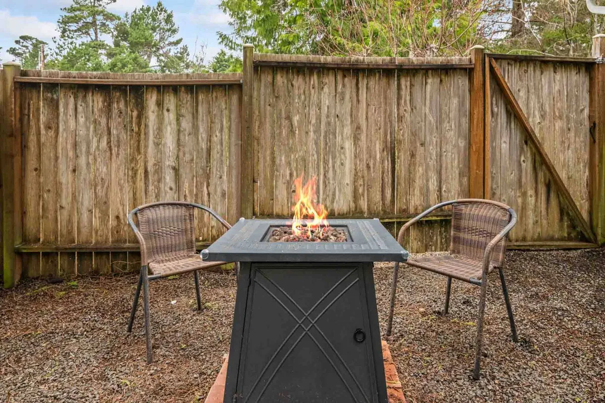 This image features a cozy fire pit surrounded by inviting chairs and enclosed by a wooden fence. The scene is set for socializing and relaxing outdoors, with the fire pit serving as a focal point for gatherings and storytelling.
